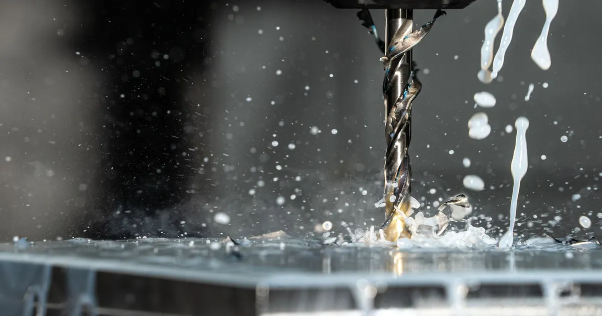Twist drill cutting into a metal plate with coolant splashing at the hole, a typical setup for drilling Inconel