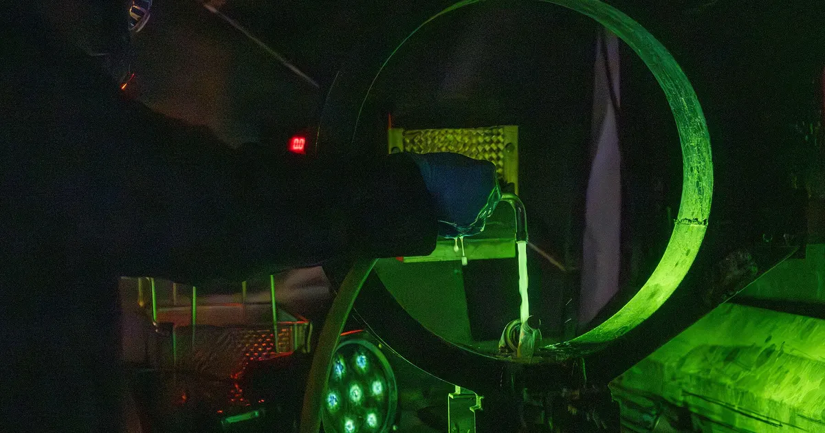 Part glowing green under ultraviolet light in a darkened booth during a fluorescent penetrant inspection