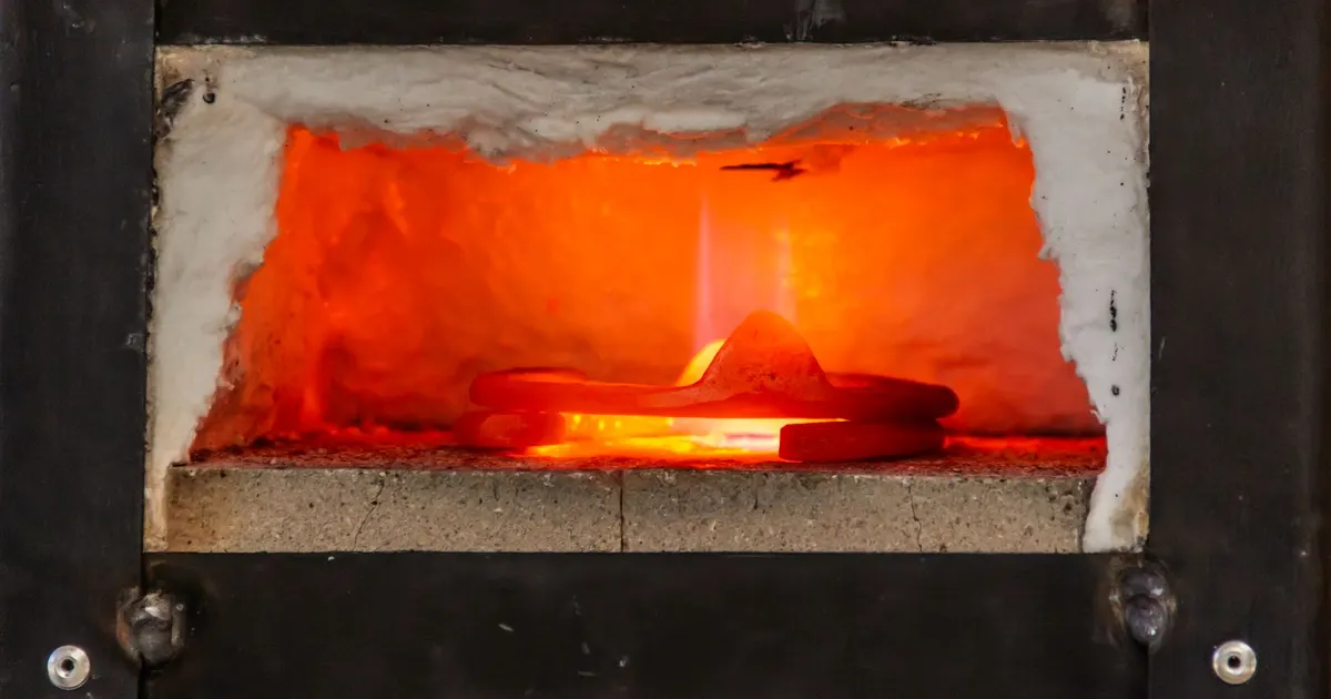 Glowing hot metal part inside a small industrial furnace chamber, a generic view of high-temperature heating