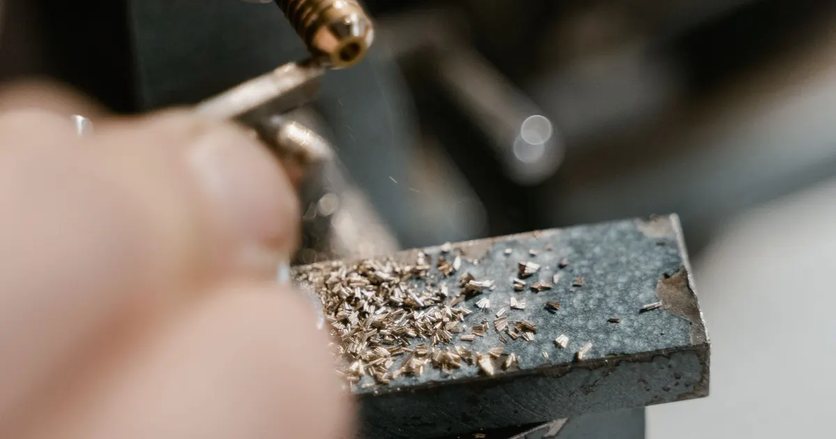 Close view of a hand holding a machined metal part with fine chips on its surface, showing the surface left after machining